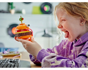 Young girl laughs, holding a LEGO Durrr Burger model with an eye and green pickle on top.