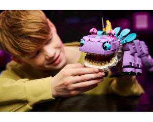 Young boy smiling, holding a purple LEGO Fortnite Klombo creature with blue eyes, open mouth showing teeth, and colorful back details.
