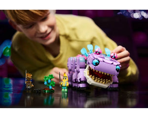 A child plays with the LEGO Fortnite Klombo set, featuring a large purple dinosaur creature, two minifigures, and a tree.