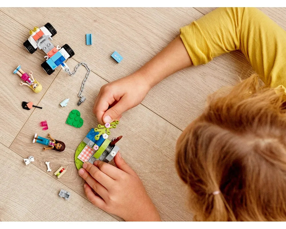 A child plays with LEGO Friends 41442 Vet Clinic Rescue Buggy, mini-dolls, and accessories on a wooden floor.