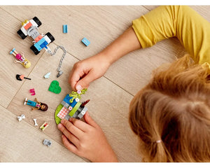A child plays with LEGO Friends 41442 Vet Clinic Rescue Buggy, mini-dolls, and accessories on a wooden floor.