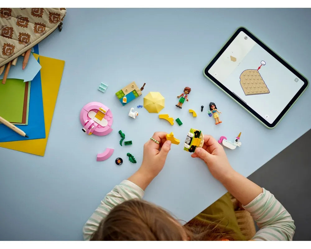Overhead view of a child building LEGO Friends 42658 Unicorn & Flamingo Pool Party, with a tablet showing instructions.