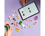Hands build LEGO Friends Puppy Playground 42665 using a tablet's digital instructions. Bricks, minifigures, and puppies on purple.