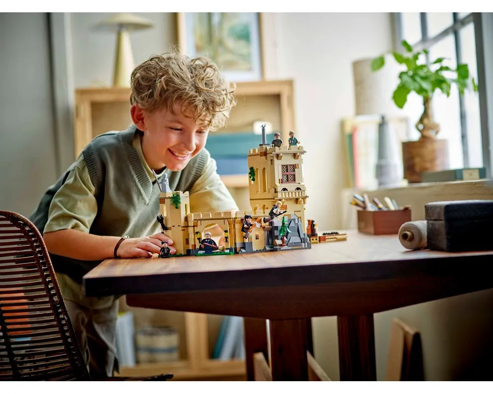 A smiling boy plays with the LEGO Harry Potter Hogwarts Castle: Flying Lessons set on a wooden table.