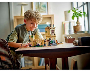 A smiling boy plays with the LEGO Harry Potter Hogwarts Castle: Flying Lessons set on a wooden table.