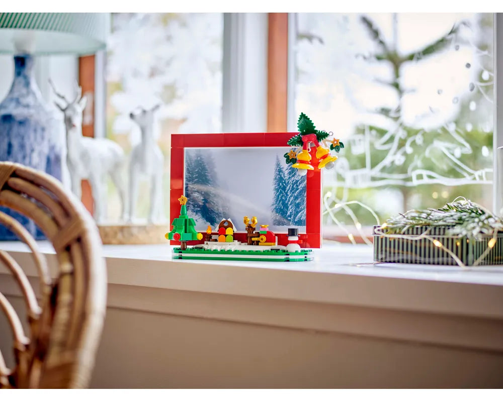 LEGO Christmas Picture Frame (40702) featuring a brick-built winter scene with a tree, barn, snowman, and festive bells.