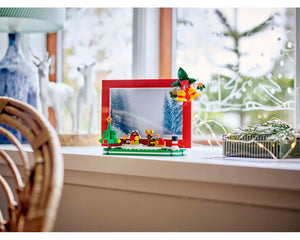 LEGO Christmas Picture Frame (40702) featuring a brick-built winter scene with a tree, barn, snowman, and festive bells.