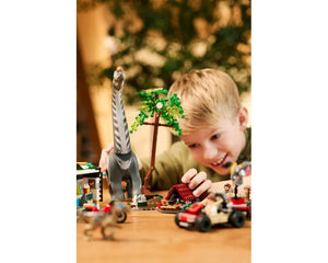 LEGO Jurassic World 76973: A boy plays with a Titanosaurus, raptor, camp, vehicles, and minifigures on a table.
