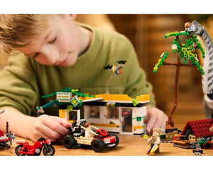 Boy plays with LEGO Jurassic World 76973 set featuring a building, buggy, minifigures, a tree, and a large dinosaur.