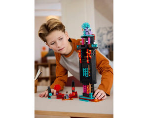A boy intently plays with a large black LEGO Minecraft 21279 Enderman Tower and smaller red and black builds on a table.