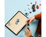 Child assembling LEGO NINJAGO 71838 Kai's Motorcycle Speed Race with digital instructions on a tablet. Minifigures and pieces are on a blue surface.
