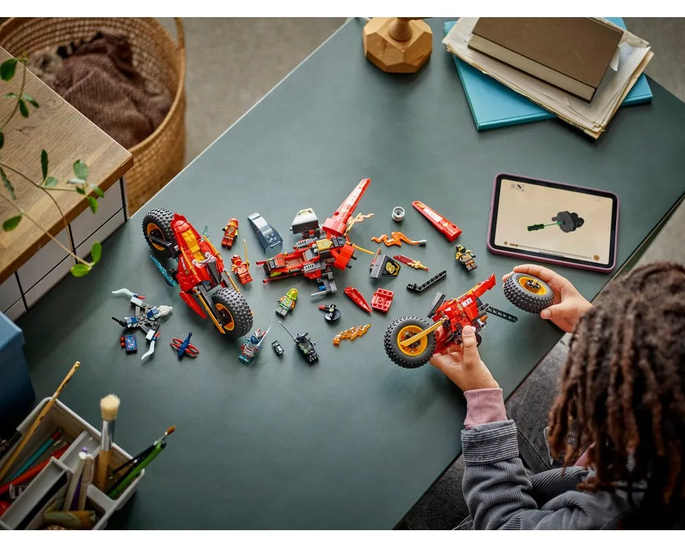 A child building a red LEGO Ninjago 71844 Ninja Combat Vehicle with digital instructions on a tablet, surrounded by minifigures and another large red LEGO vehicle.