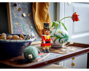 LEGO Nutcracker 40640 figure in red and gold uniform on a wooden tray with nuts, green yarn, and a vase with a flower.