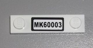 White LEGO modified 1x4 plate with 2 studs and a black sticker displaying 'MK60003' in white text.