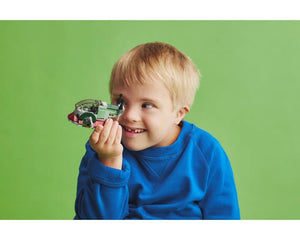 Young boy smiles, holding a LEGO Star Wars Boba Fett's Starship Microfighter 75344 to his eye against a green background.