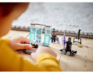Child's hands playing with LEGO Super Heroes Shuri's Lab (76212) set, featuring Shuri and Black Panther minifigures.