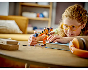Young girl with orange glasses playing with an orange and black LEGO Rocket Mech Armor (76243) on a wooden table.