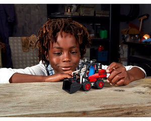Young child admiring a red, blue, and black LEGO Technic 42116 Skid Steer Loader model on a wooden table.