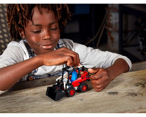 Child playing with a red and black LEGO Technic 42116 Skid Steer Loader on a wooden table.
