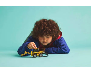 Young child playing with a yellow LEGO Technic 42197 Backhoe Loader on a blue background.