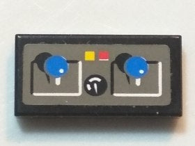 A black LEGO 1x2 tile with a grey pattern featuring two blue joysticks, a central knob, and yellow and red buttons.