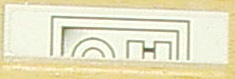 Close-up of a light gray LEGO 1x4 tile with a dark gray pattern of half-circles and rectangles within a rectangular border.